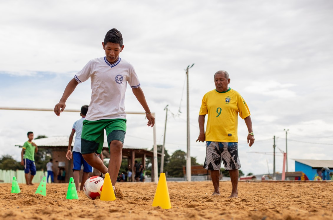 Menino joga futebol Menino joga bola em um campo de areia
