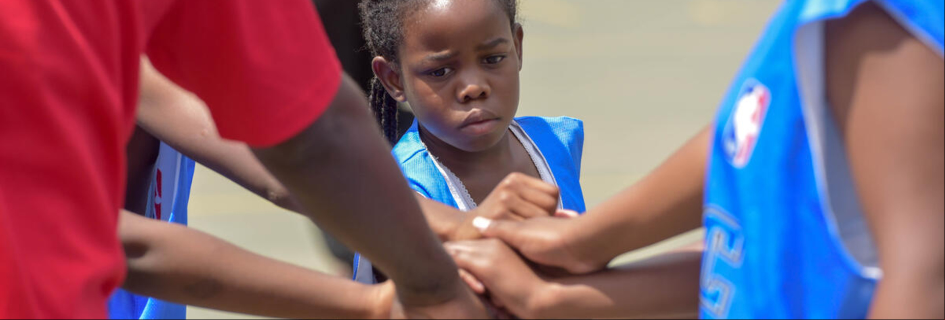 Un grupo de personas afrodescendientes unen sus manos con las de una niña que lleva puesto un chaleco azul Un grupo de personas afrodescendientes unen sus manos con las de una niña que lleva puesto un chaleco azul