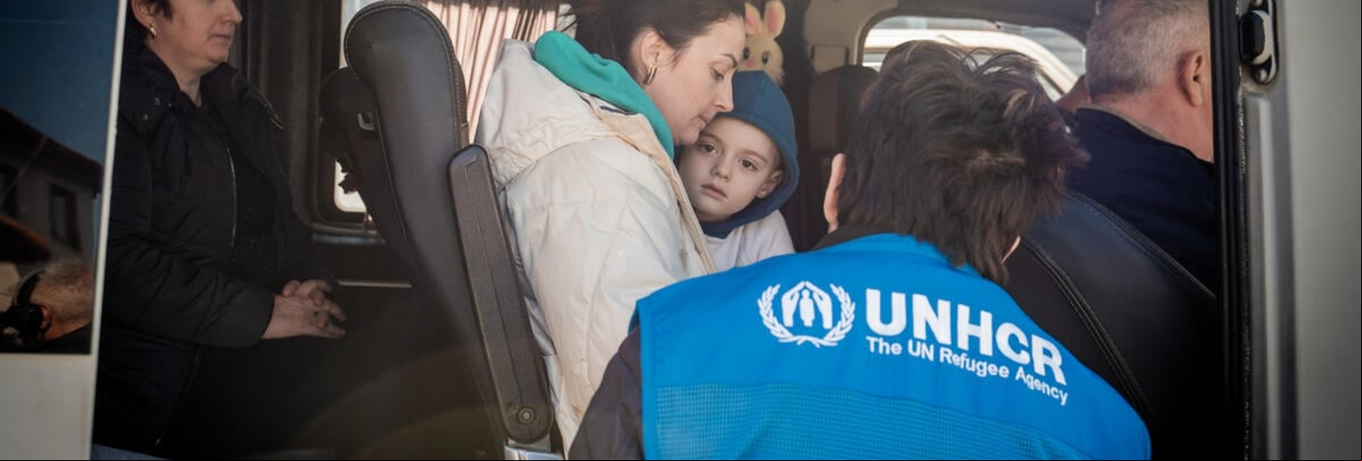 Las personas refugiadas que huyen de Ucrania cruzan la frontera de Eslovenia con Italia Un trabajador de ACNUR charla con un chico y una refugiada de Ucrania en un autobús.