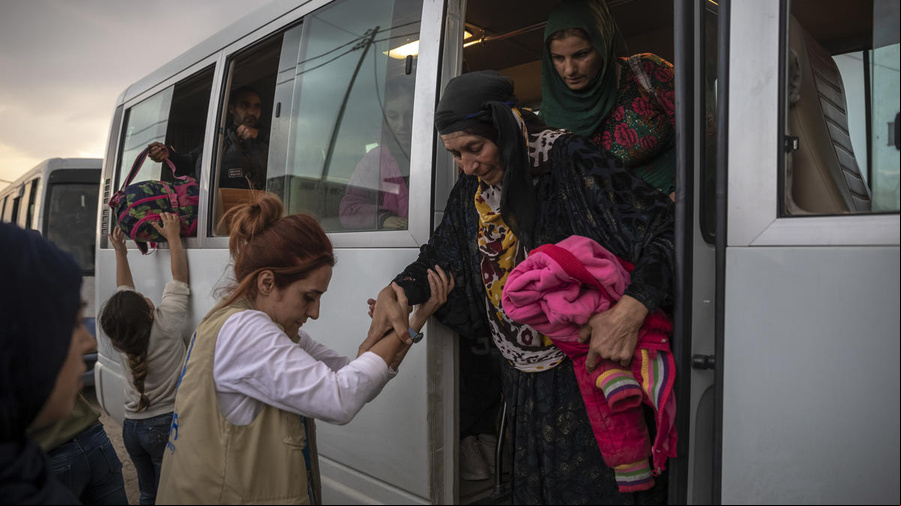 Una trabajadora de ACNUR ayuda a una refugiada mayor de Siria a bajar de un autobús.