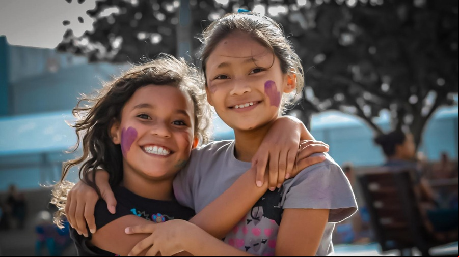 Dos niñas se abrazan sonriendo en un día soleado.