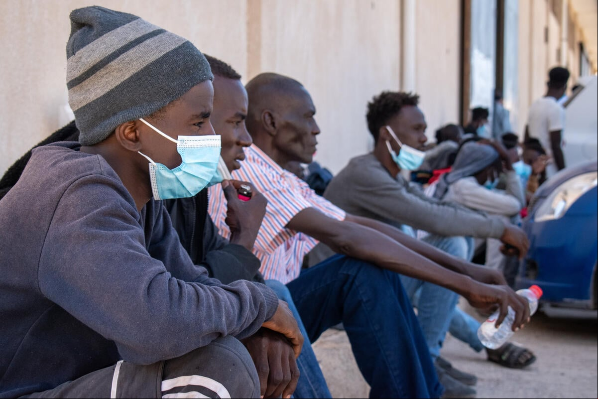 Una fila de hombres sentados en el suelo frente a un centro de la ONU