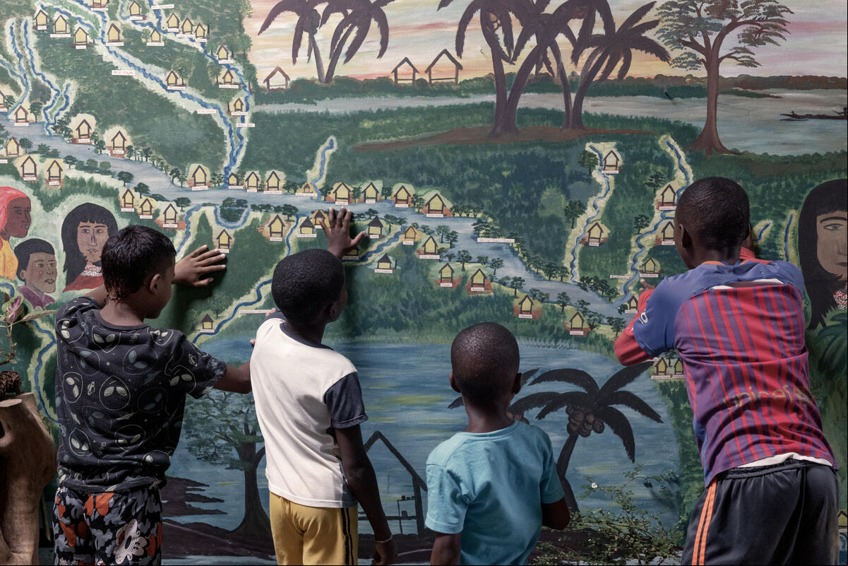 Un grupo de niños observan un mural que representa a las comunidades que viven junto a un río.