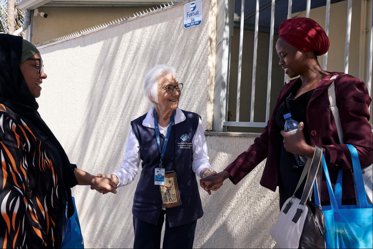 Tres mujeres sonrientes se dan la mano en el exterior de un edificio