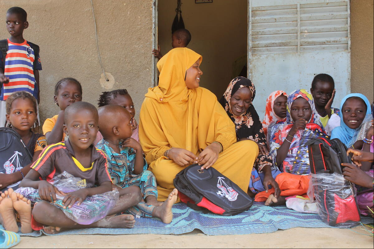 Una mujer que lleva puesta una indumentaria color amarillo canario está sentada en medio de un grupo de niños en Burkina Faso
