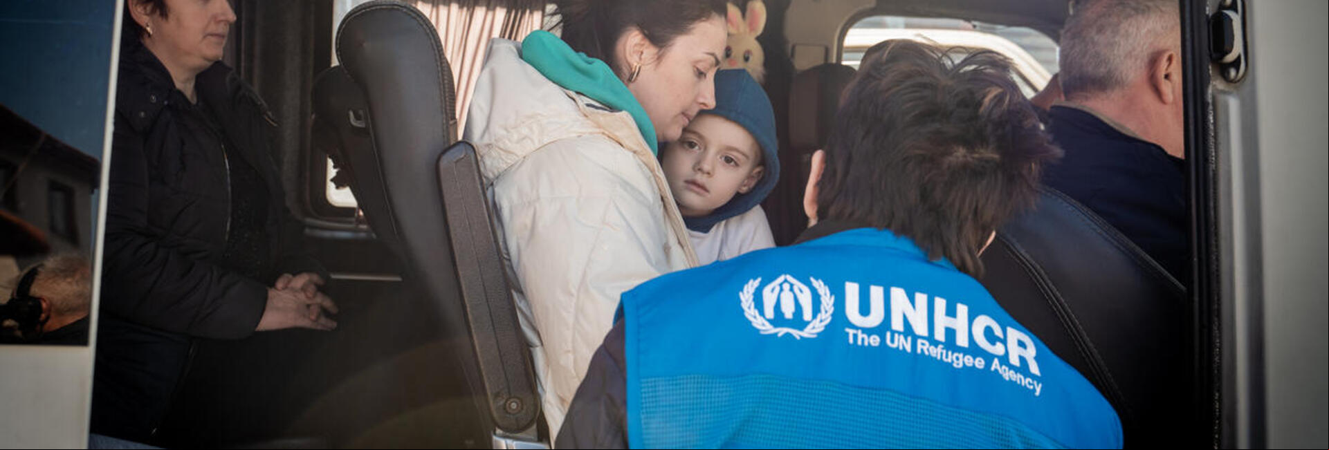 Las personas refugiadas que huyen de Ucrania cruzan la frontera de Eslovenia con Italia Un trabajador de ACNUR charla con un chico y una refugiada de Ucrania en un autobús.