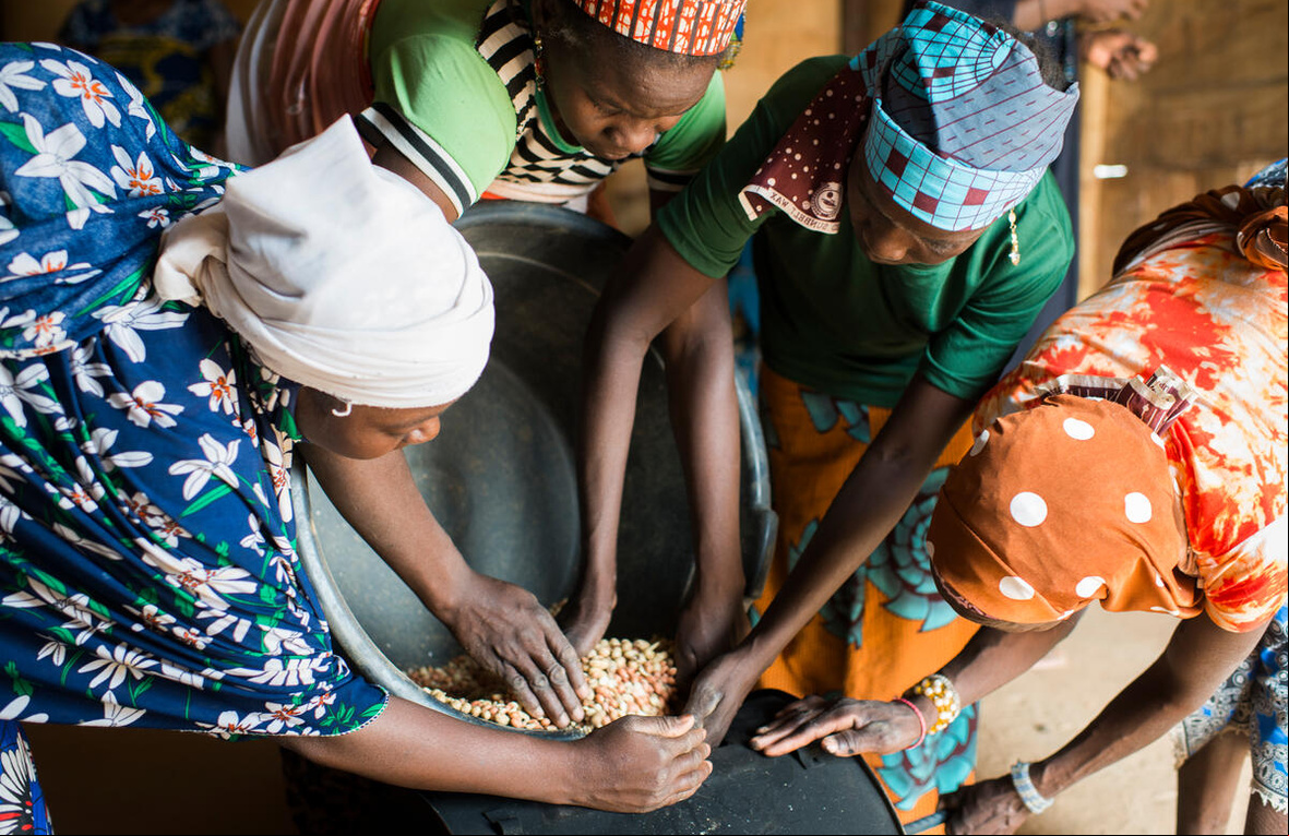 Cuatro mujeres, de Nigeria y de Níger, maniobran con una olla con granos para elaborar crema de maní