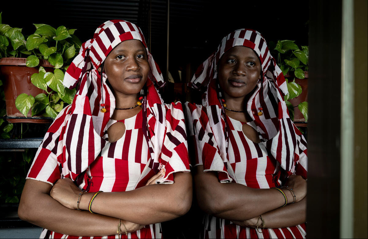 Una mujer de Burkina Faso, que lleva puesto una indumentaria de color blanco y rojo, mira a la cámara con los brazos cruzados sobre su abdomen