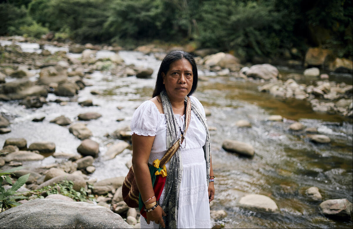 Una mujer de cabello oscuro vestida de blanco junto a un río.