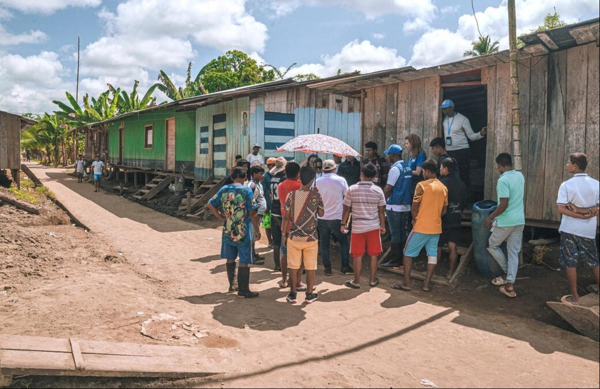 Un grupo de personas reunidas fuera de una casa en un area rural interactuando con funcionarios de ACNUR.