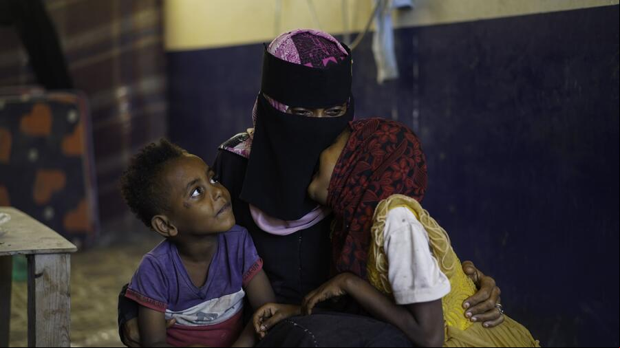 Una mujer con un hijab que cubre todo su rostro, excepto los ojos, abrazo a un niño y a una niña