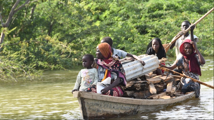 Varios adultos y niños viajan en una canoa apilada con madera y hierro ondulado.