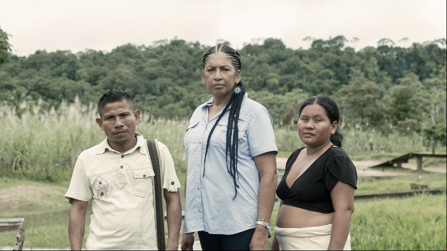 Un hombre y dos mujeres frente a un arroyo al borde de una selva tropical.