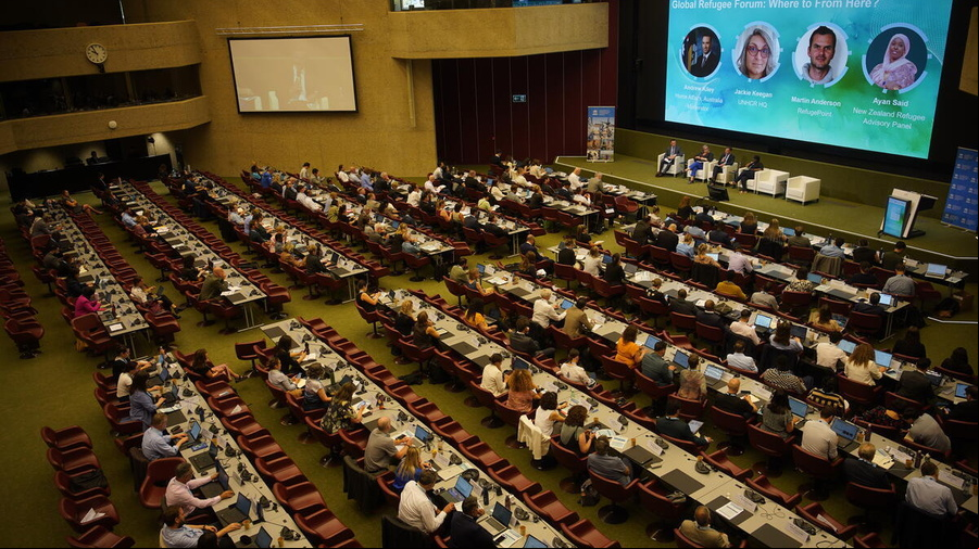 Imagen de un auditorio repleto de personas; al frente, un y una pantalla en la que se está proyectando una presentación