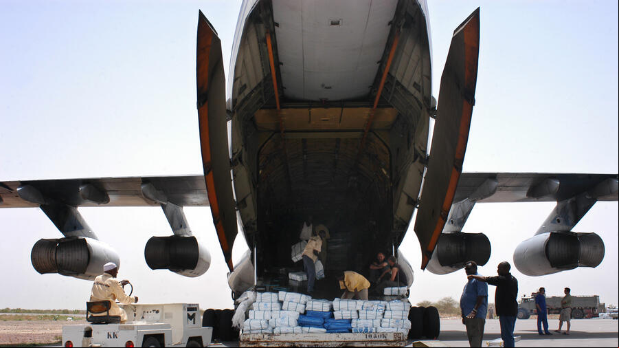 Imagen de la parte posterior de un avión de carga; un grupo de personas están subiendo suministros con el logotipo de ACNUR Imagen de la parte posterior de un avión de carga; un grupo de personas están subiendo suministros con el logotipo de ACNUR