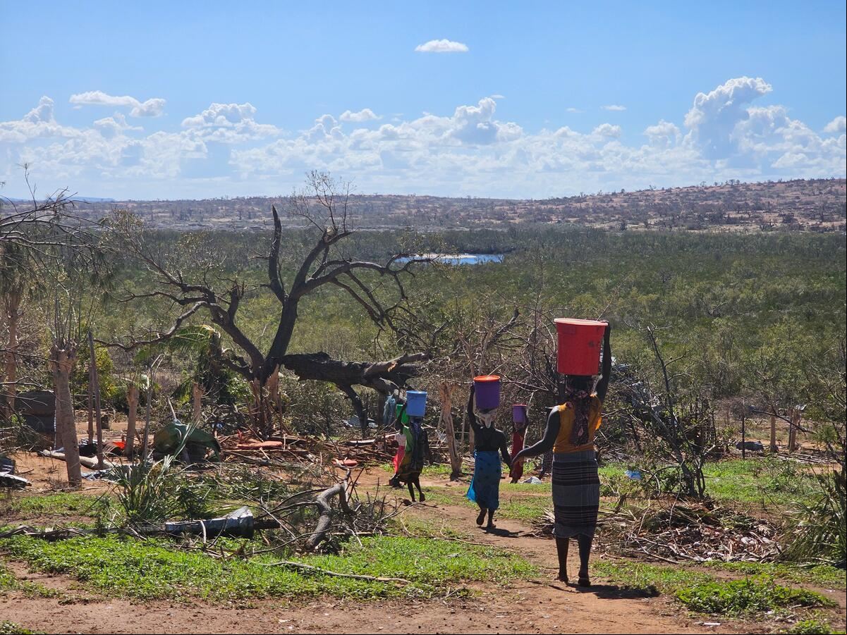 Un grupo de mujeres caminan por un sendero rural cargando baldes de agua en sus cabezas.